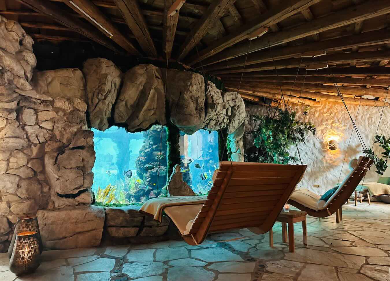 Ruhebereich bei den Massage- und Behandlungsräumen des Stanglwirt mit Holzliegen, Natursteinwänden und Aquarium.