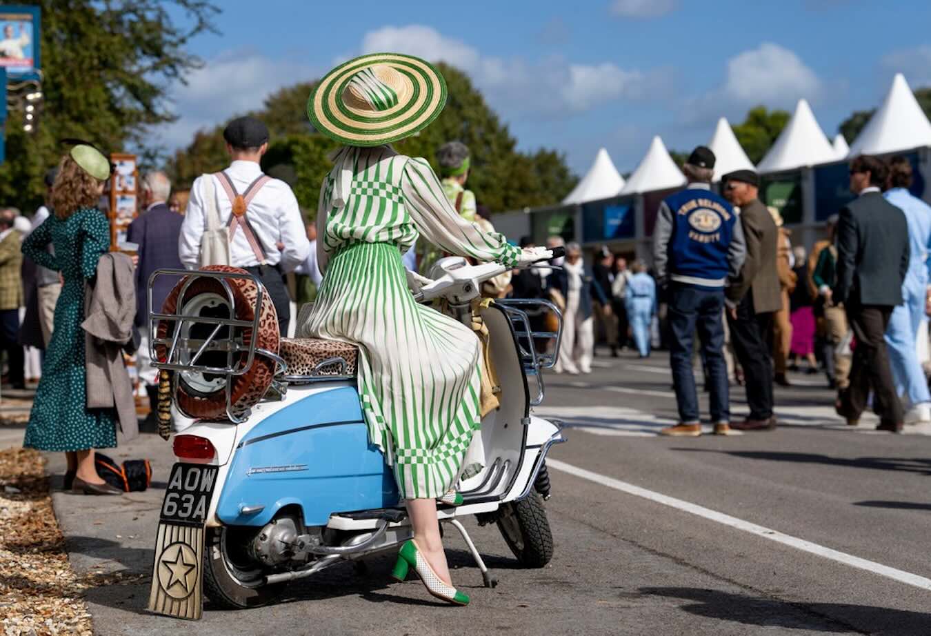 Besucherin in grün-weißem Vintage-Kleid auf einer blauen Vespa beim Goodwood Revival 2026