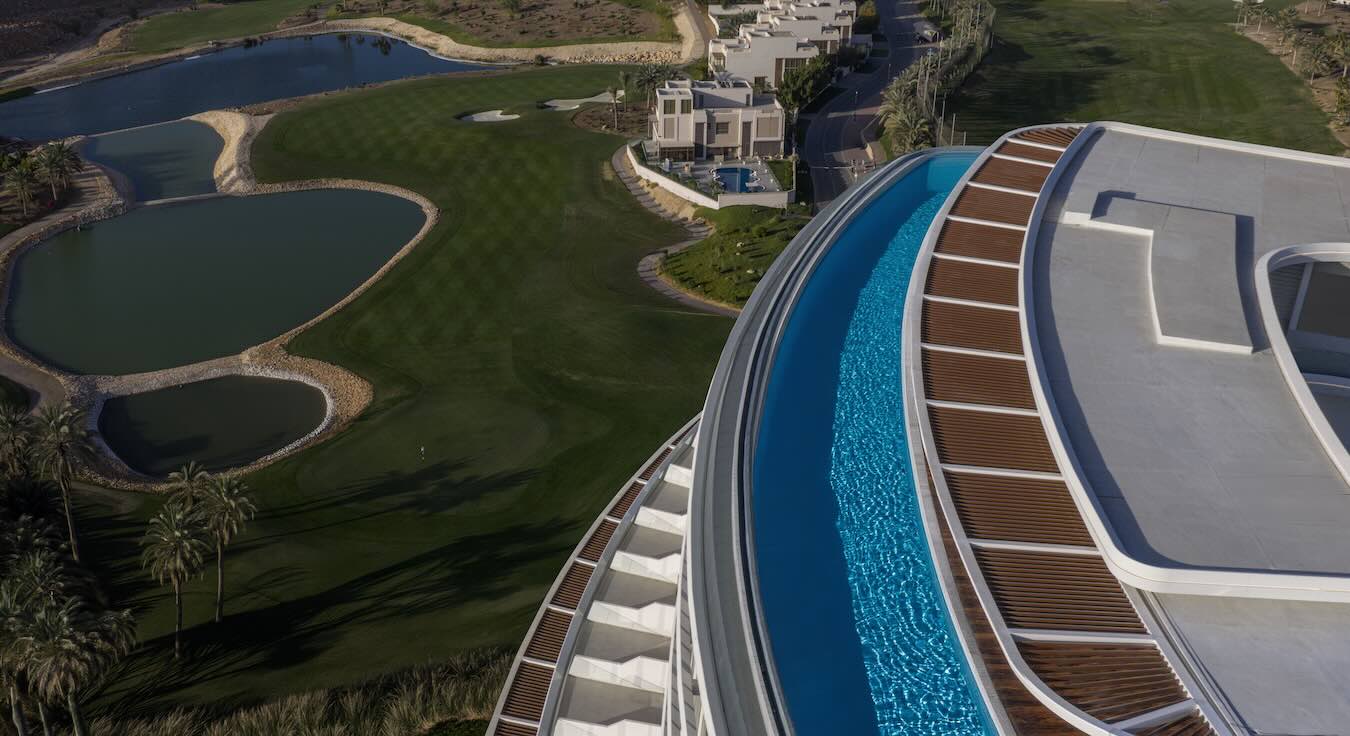 Luftaufnahme des geschwungenen Rooftop-Pools am Tivoli LA VIE Muscat mit Blick auf den Golfplatz und seine Wasserhindernisse.